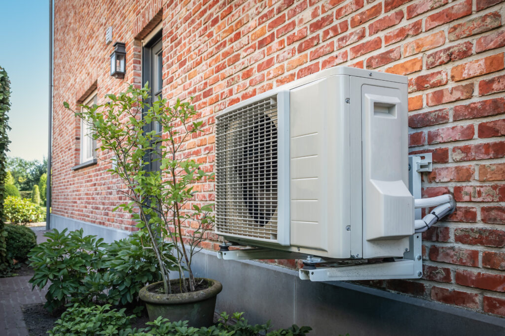 Domestic heat pump unit mounted on a brick house wall.