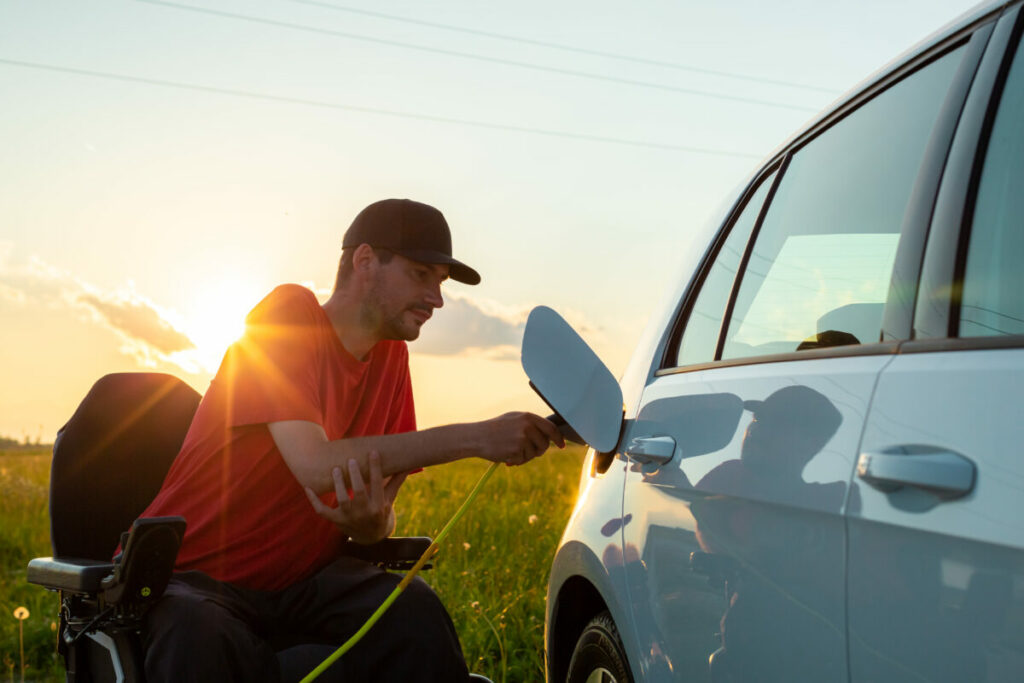 Man in wheelchair plugging in a charger in an electric car. Image: AdobeStock