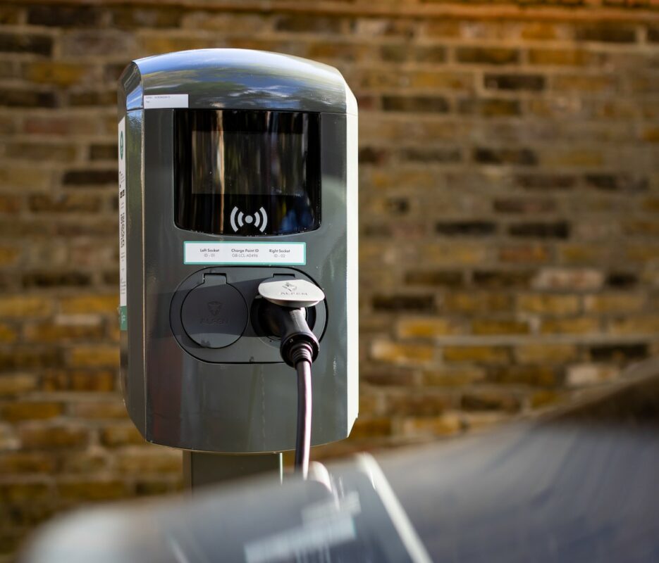 Public EV car charger on street with brick wall in the background and car in the foreground