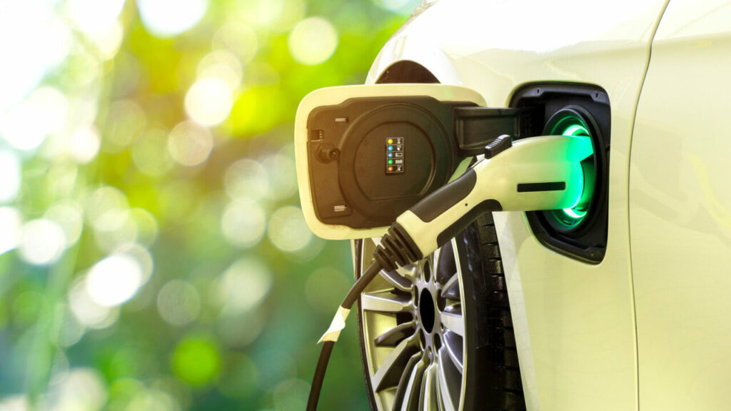 Yellow EV car plugged into charger with greenery in the background