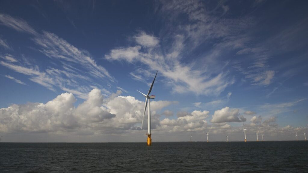 An offshore wind turbine underneath a blue sky with white clouds