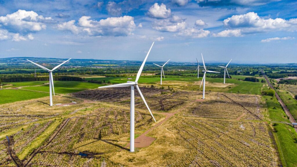 Wind turbines surrounded by green and yellow fields under a blue sky with big white clouds