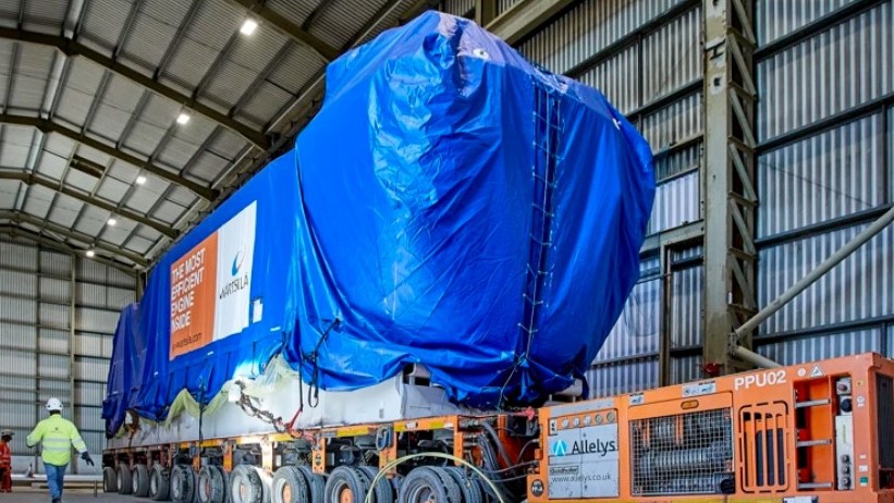A large truck carries an engine covered by blue tarpaulin