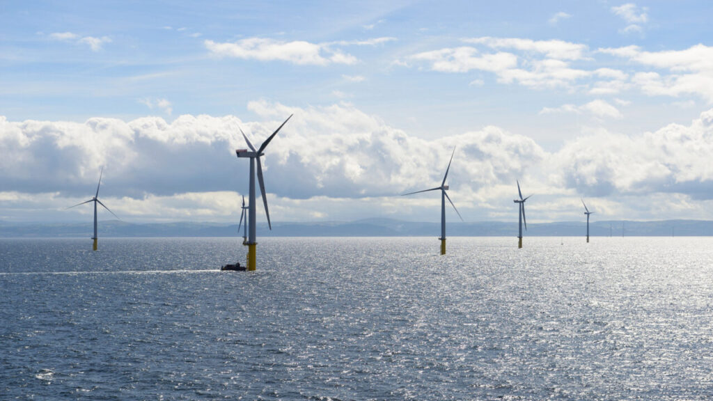An offshore wind farm under a blue sky with puffy white clouds
