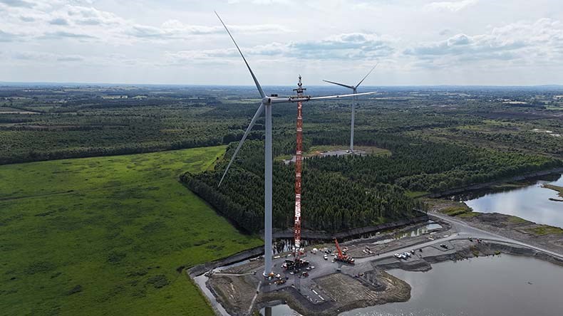 A wind turbine stands next to a crane working to install it.