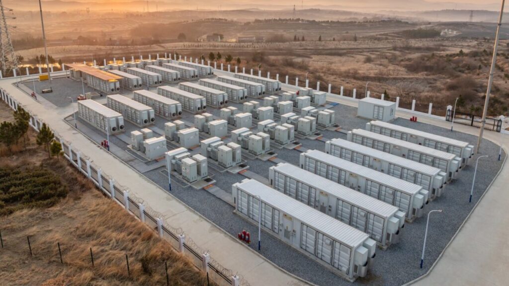 A series of large battery storage units under a setting sun