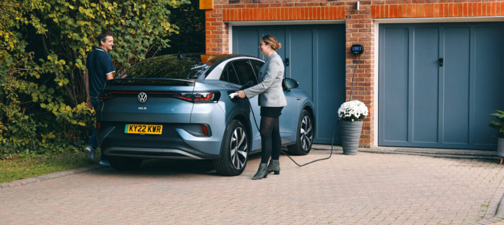 Volkswagen electric vehicle outside private garage with a woman using an EV charger and a man on the other side of the car.