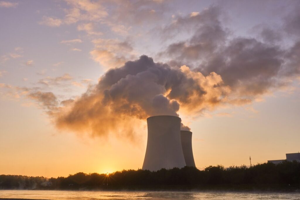 a nuclear cooling tower with steam pouring out of it, at sunset