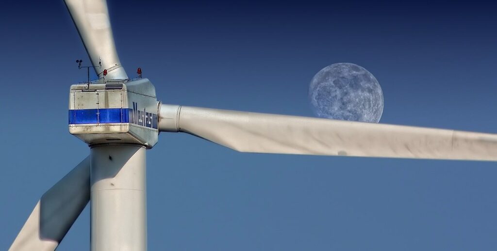 A close up of blades on a wind turbine in front of a blue sky and a faint view of the moon