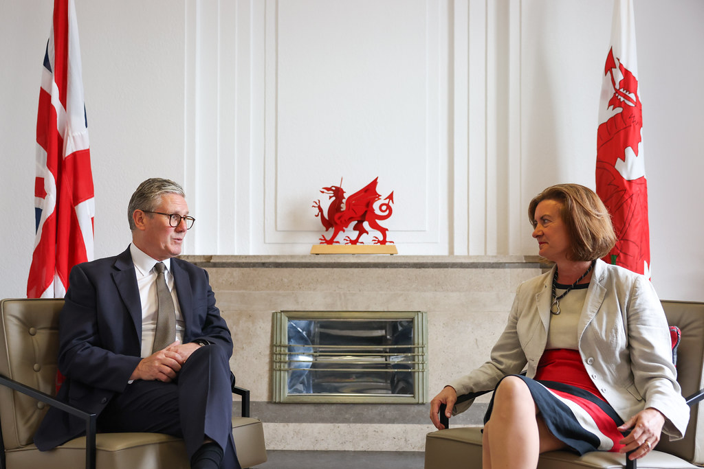 Prime Minister Kier Starmer and Welsh First Minister Eluned Morgan sit opposite each other in chairs in a white room in front of UK and Welsh flags