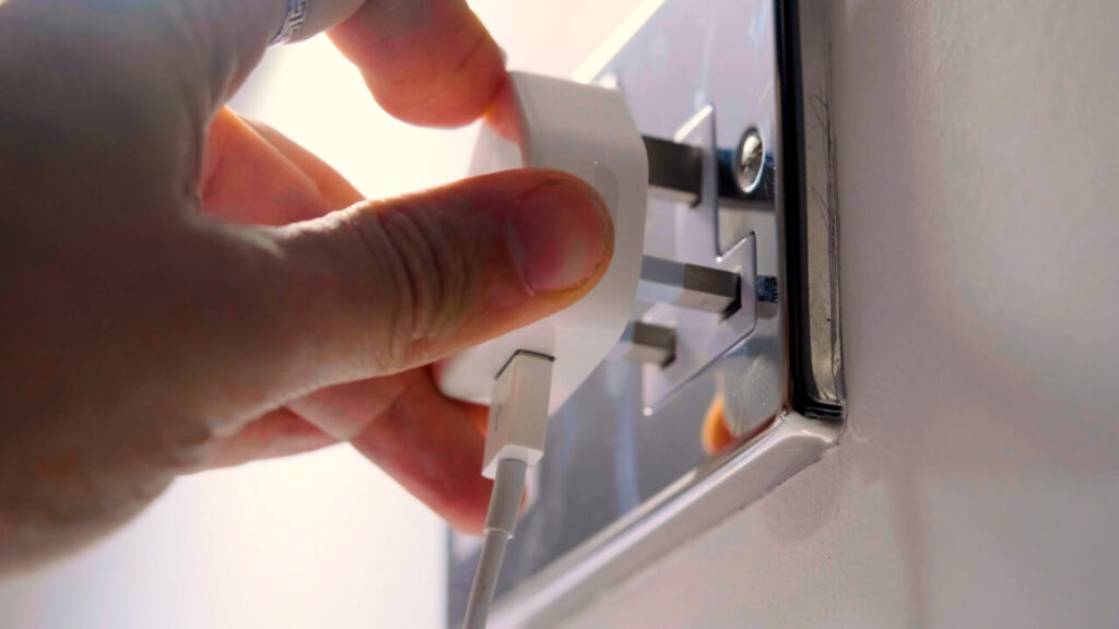 A hand plugs a charger into a plug socket
