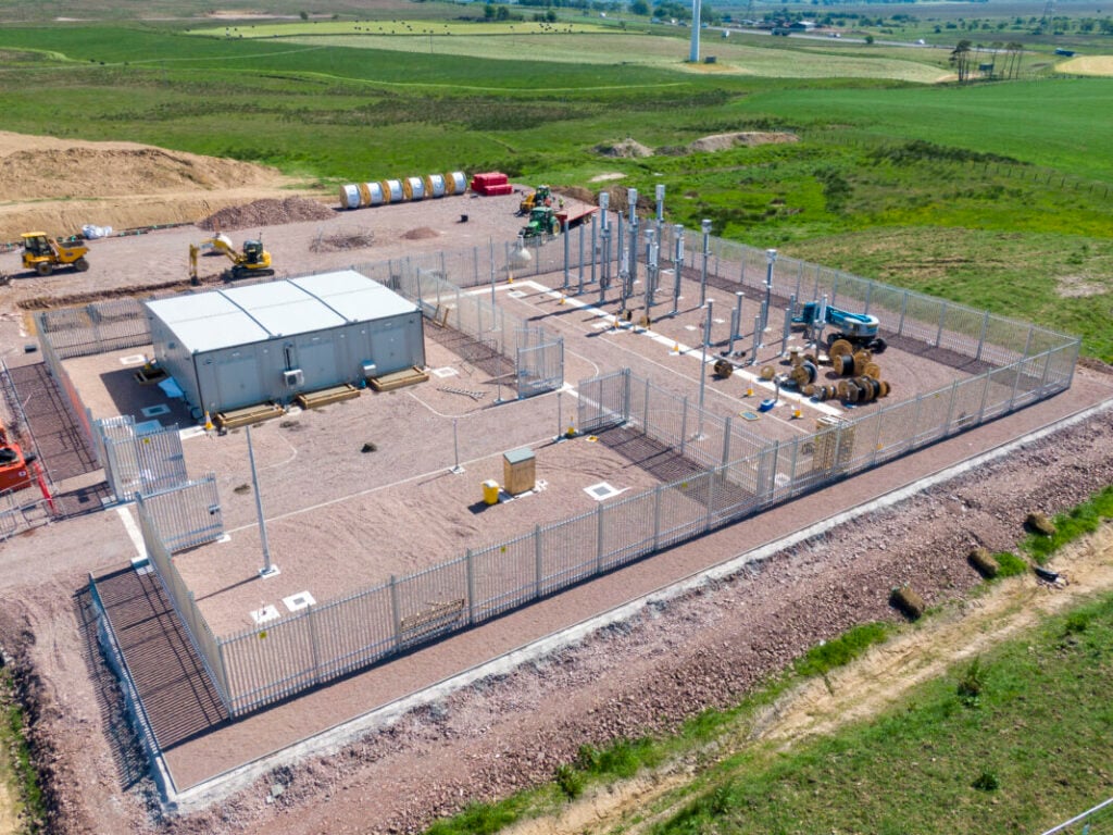 An electric substation viewed from above, surrounded by green fields