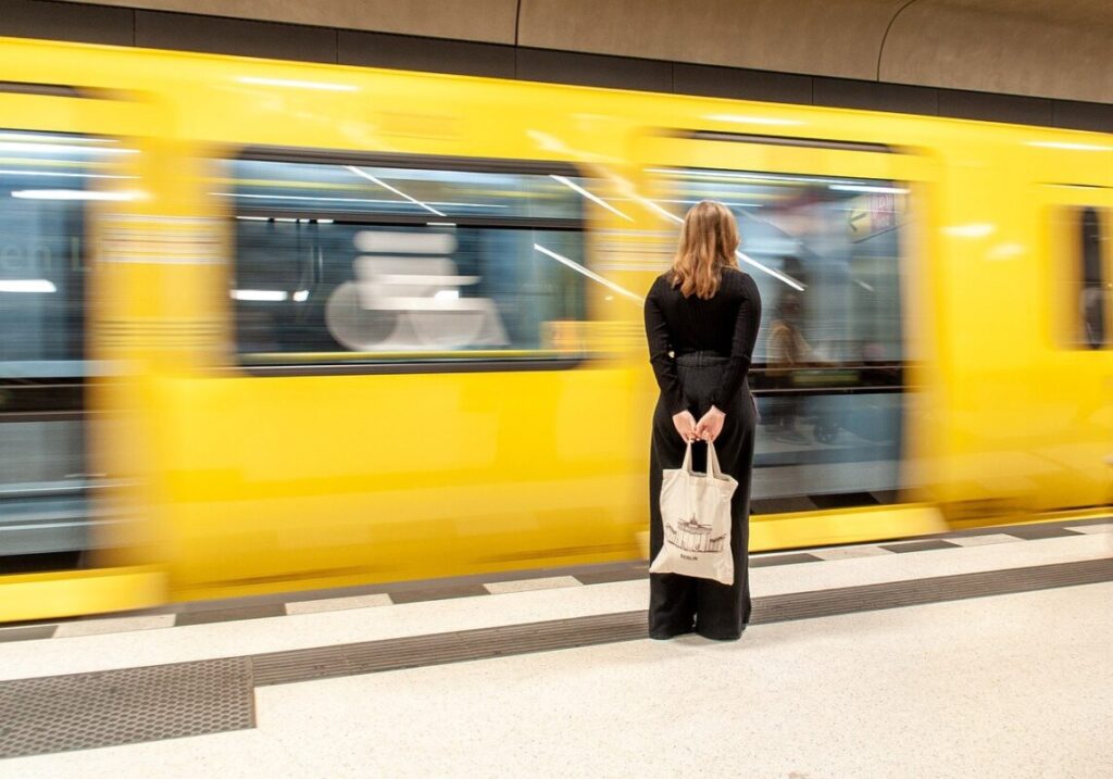 A woman stands in front of a bright yellow subway train