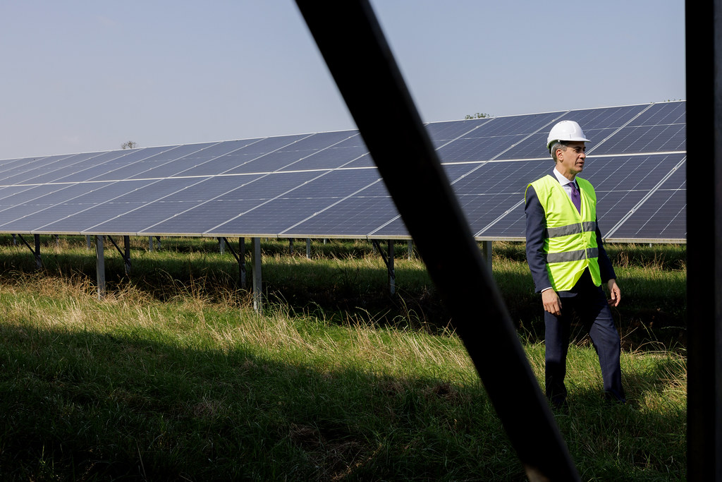 Ed Miliband walks next to solar panels in a hi ves vest and helmet