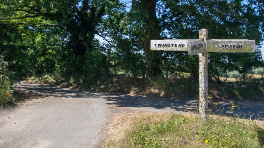 A country road with an old fashioned road sign pointing out the town of Twinstead