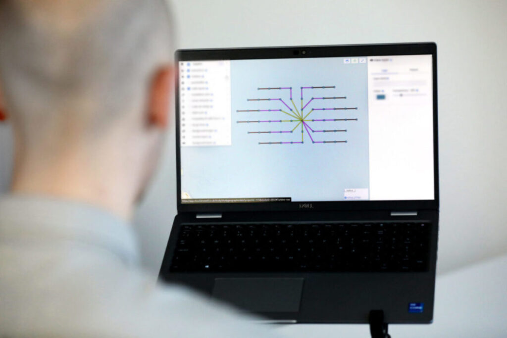 A man, out of focus and with his back to the camera, uses cable planning software on a laptop