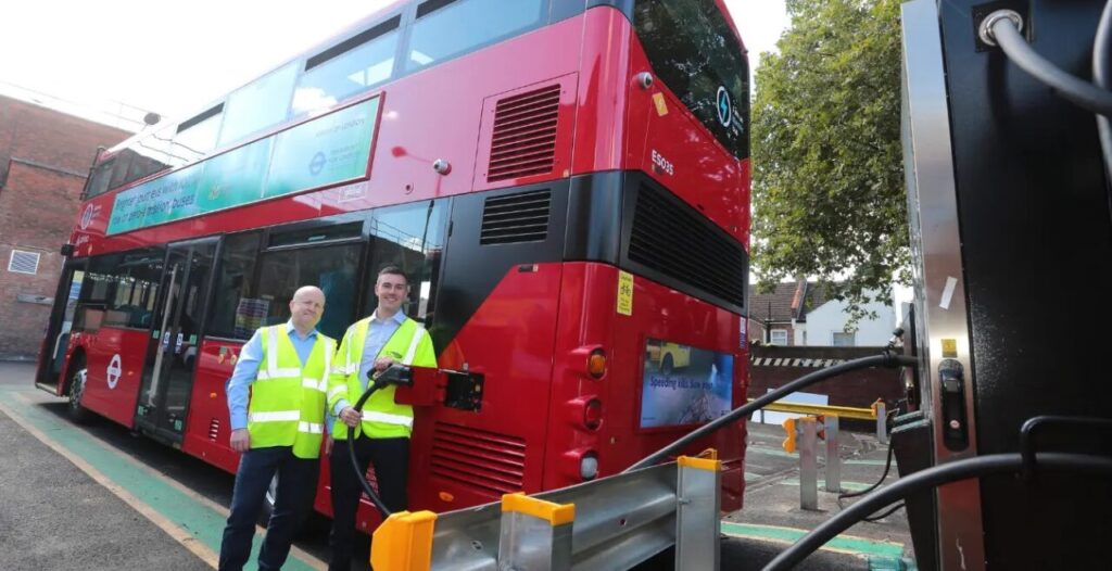 Two men in high vis stand next to an electric london bus