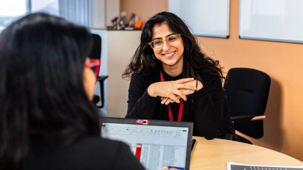 two west Asian women look at eachother over laptop screens while smiling
