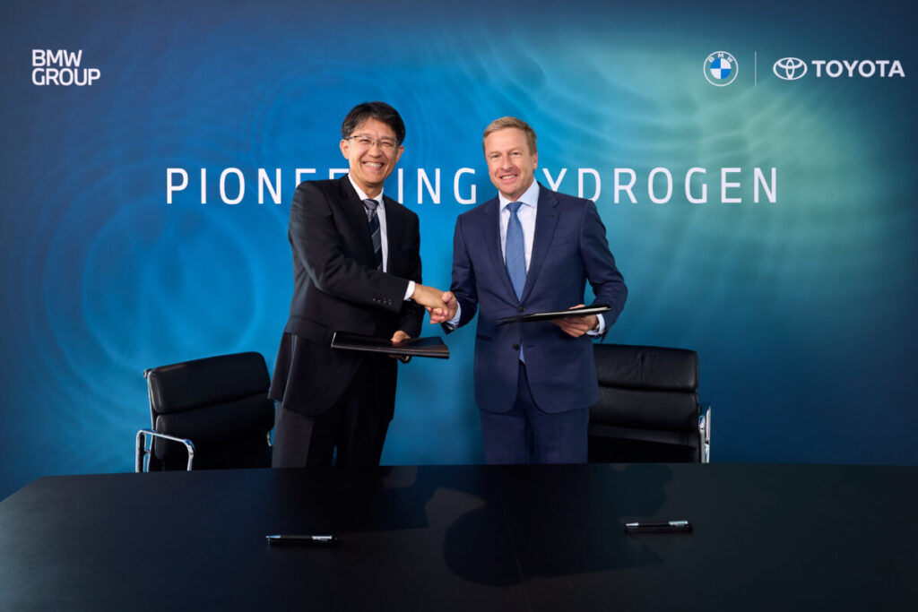 An Asian man and a white man shake hands in front of a blue background after a successful business deal