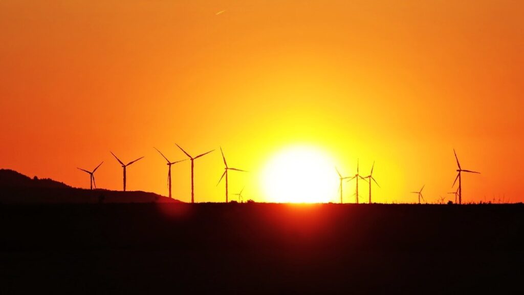 Wind turbines on a hill in the distance, silhouetted against an orange sunset