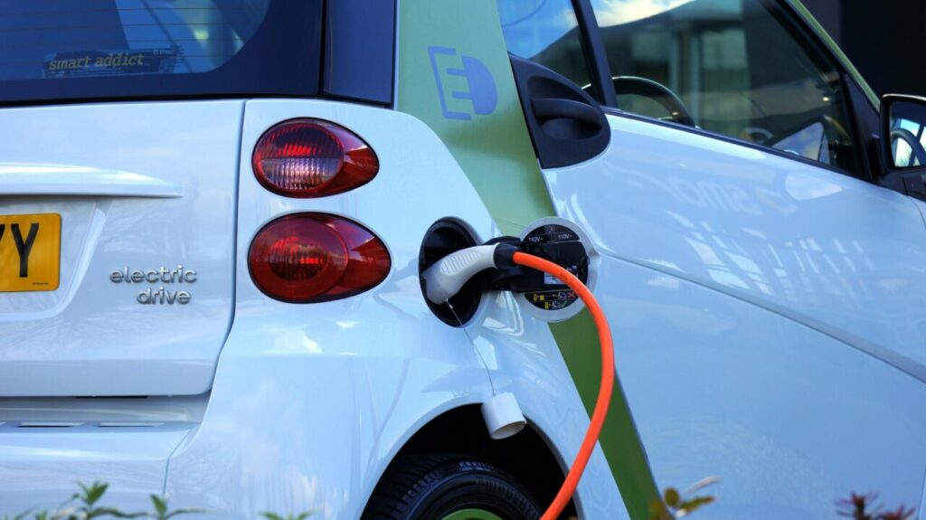 a white electric car plugged into an orange charging cable