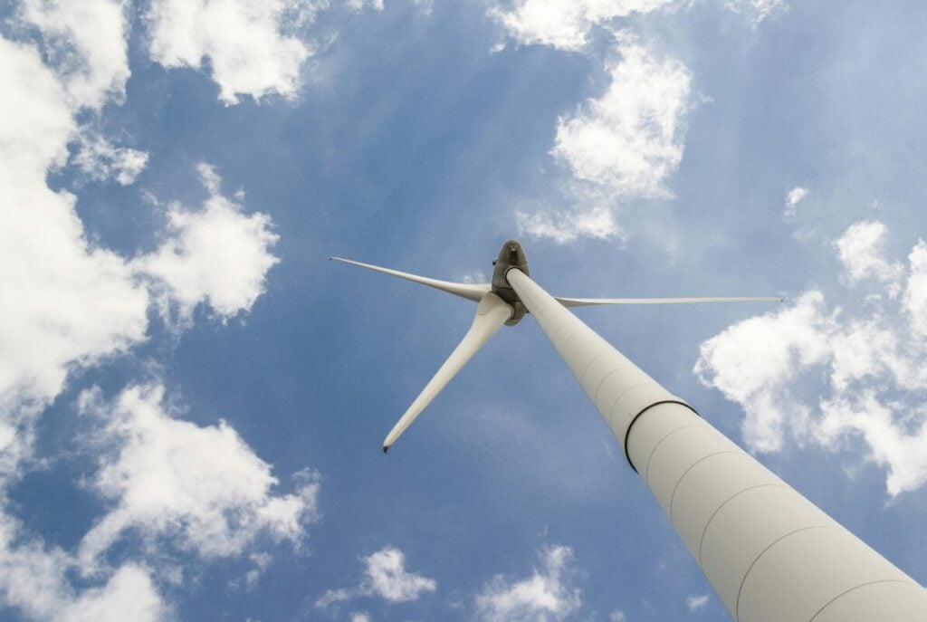 A white wind turbine, shot from below, under a blue sky