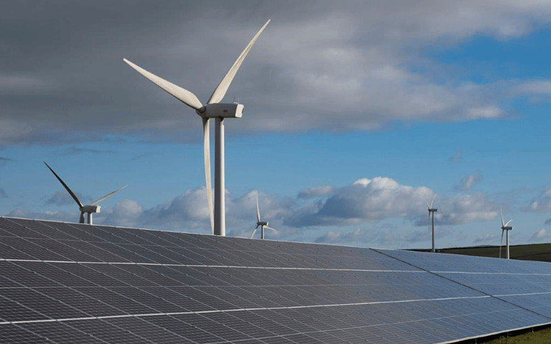 Solar panels sit in front of a wind turbine