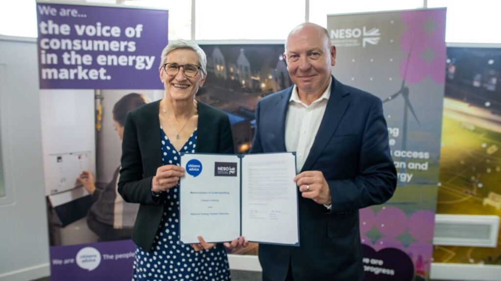 An older white woman and a bald white man hold a booklet together and smile at the camera