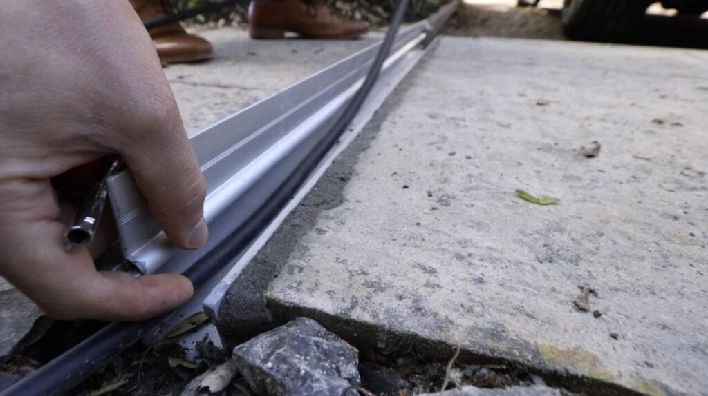 A hand lays a thin cable into a metal channel set into the ground