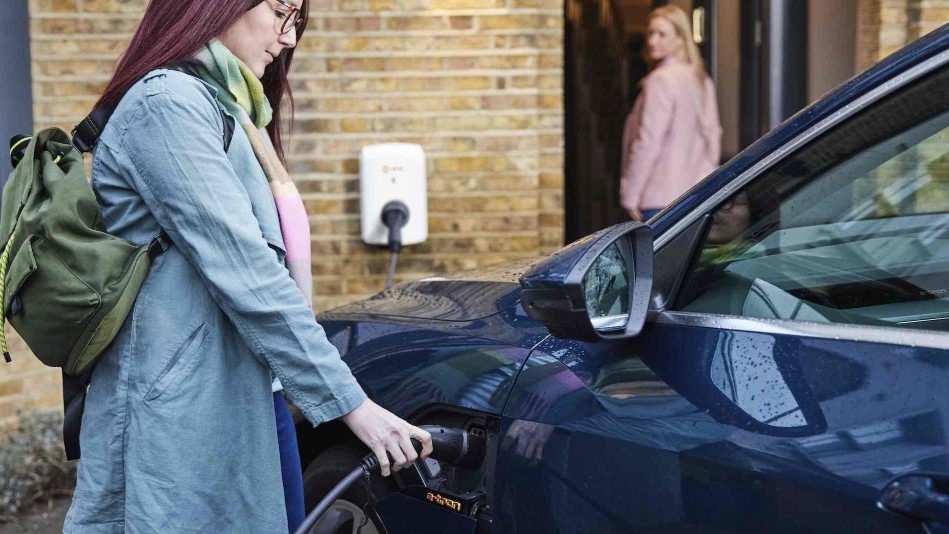 A woman plugs an EV charger into her car, with a Hive EV charger unit in the background