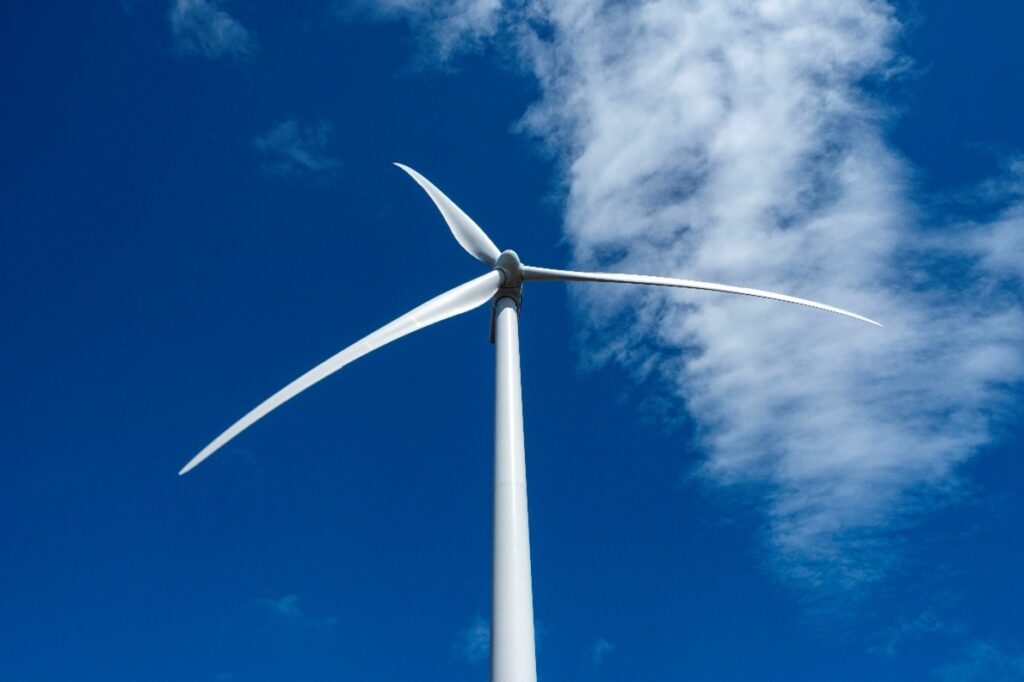 A single wind turbine in front of a bright blue sky