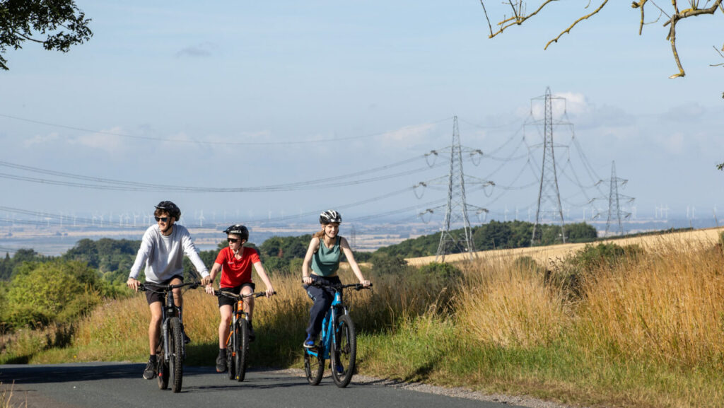 three people ride bikes with pylons behind them