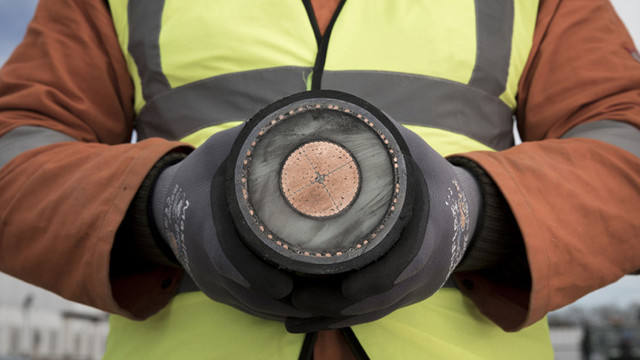 Two hands hold a large interconnector cable, cut so the cross section can be seen