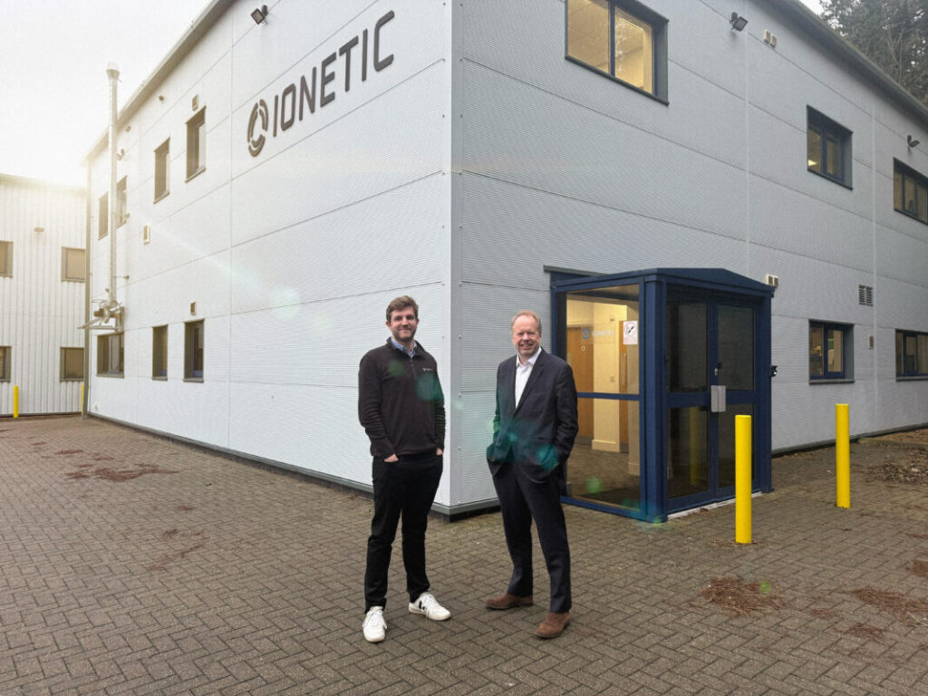 two white men stand outside of a building and smile