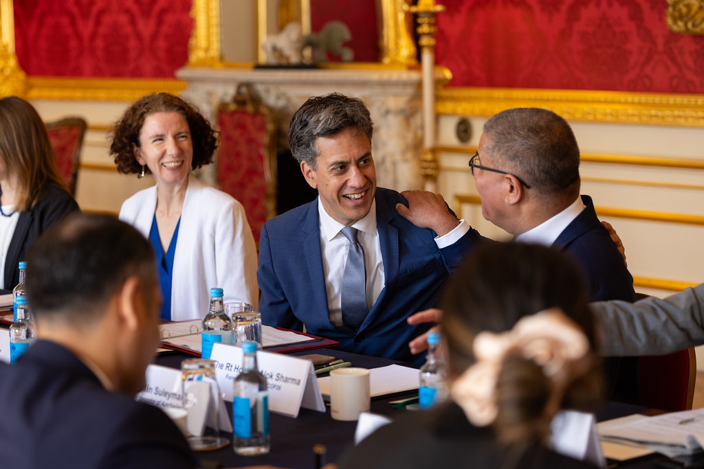 ed miliband smiles surrounded by people in a red room