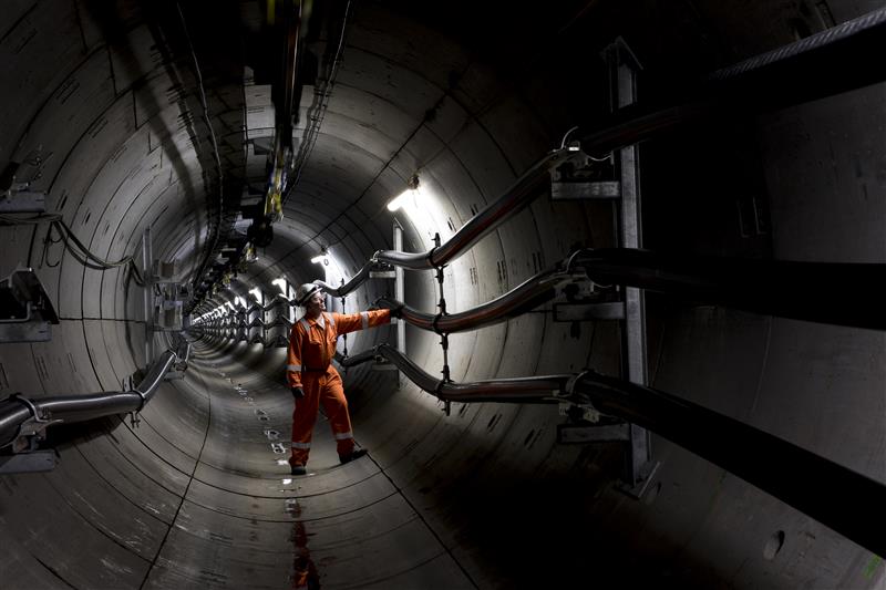 a person in a high vis vest inspects cables in a large tunnel