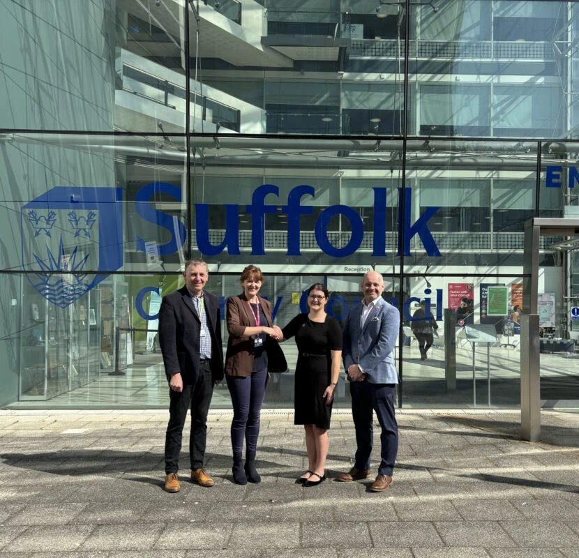 A group of people smile outside the glass fronted building of suffolk county council