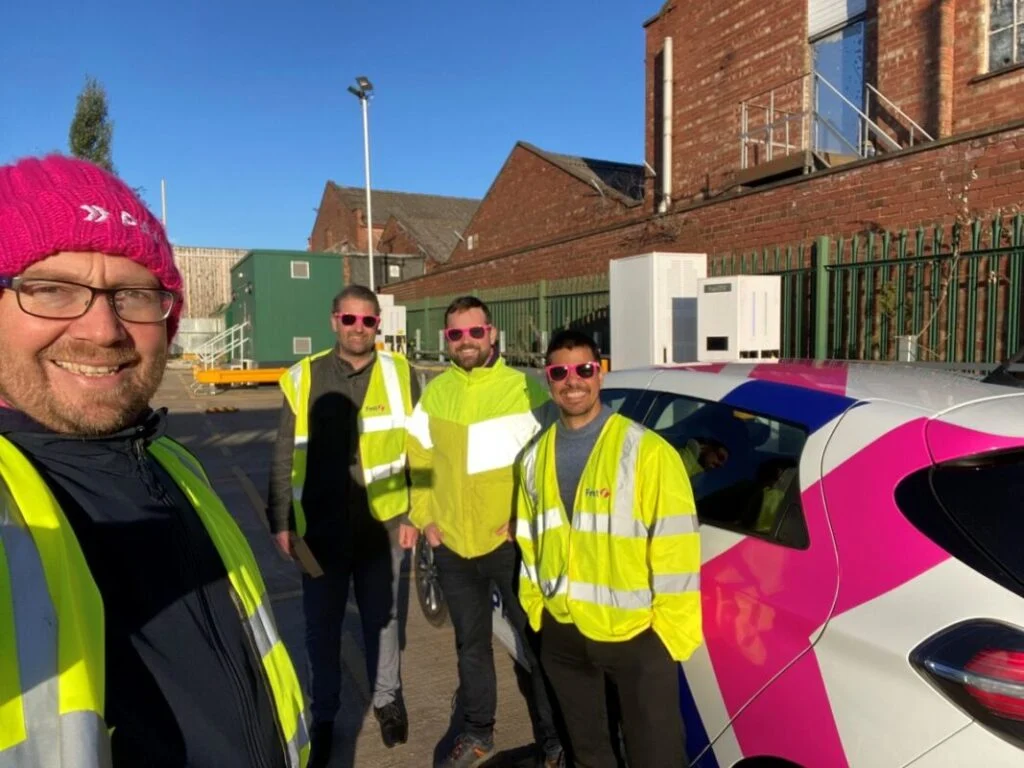 men in high vis jackets stand by a pink and white car