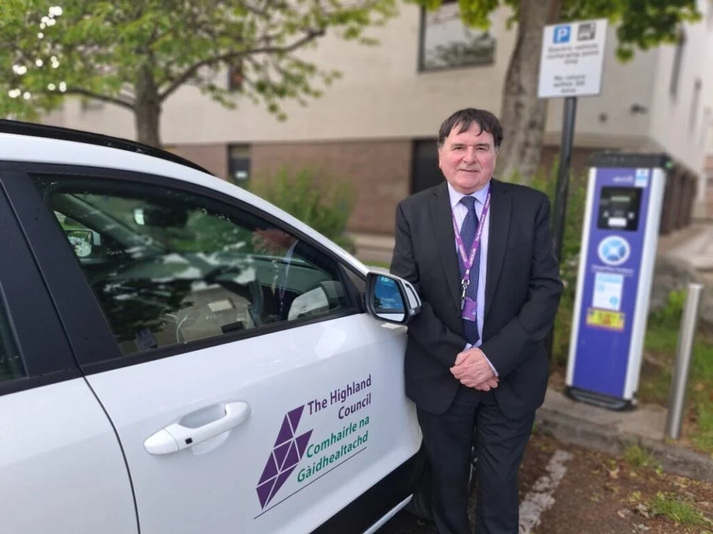 A man stands next to a white car with the highland council logo