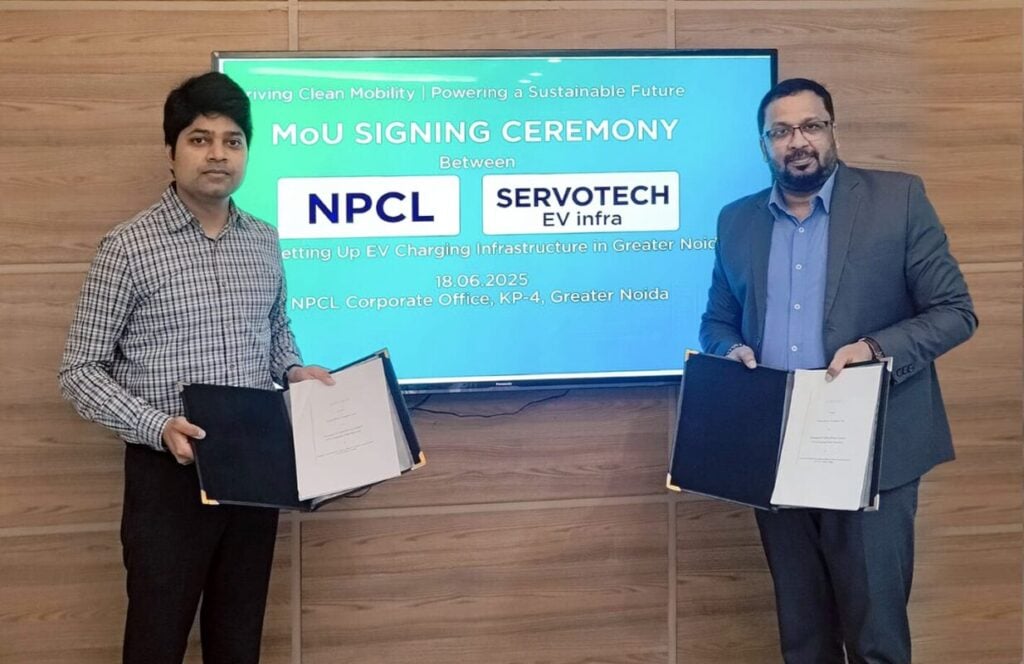 Two Indian men stand in front of a screen with documents in hand