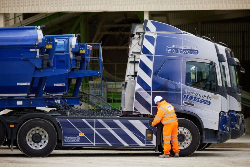 a man stands next to a large blue lorry.