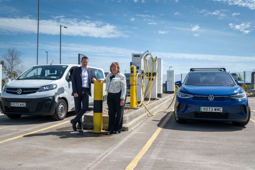 a white man and woman stand next to eachother near ev chargers.