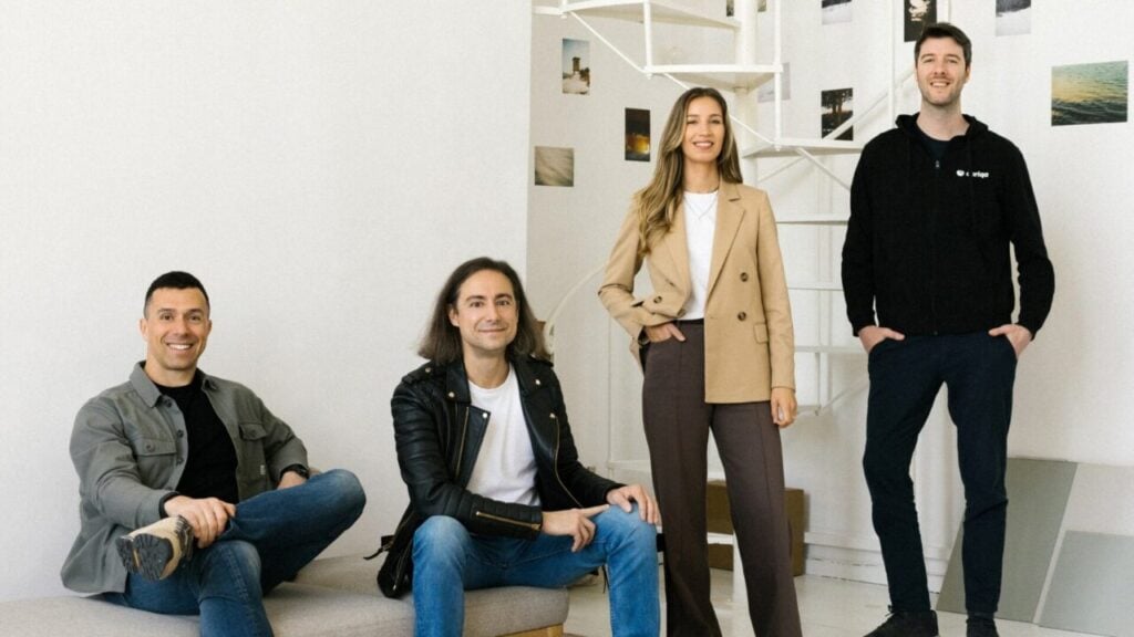 four smiling people are lined up in a row in a white room