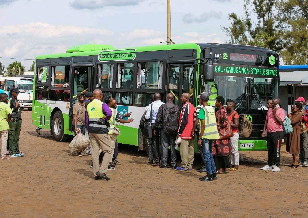 an electric bus surrounded by people on a warm dusty road