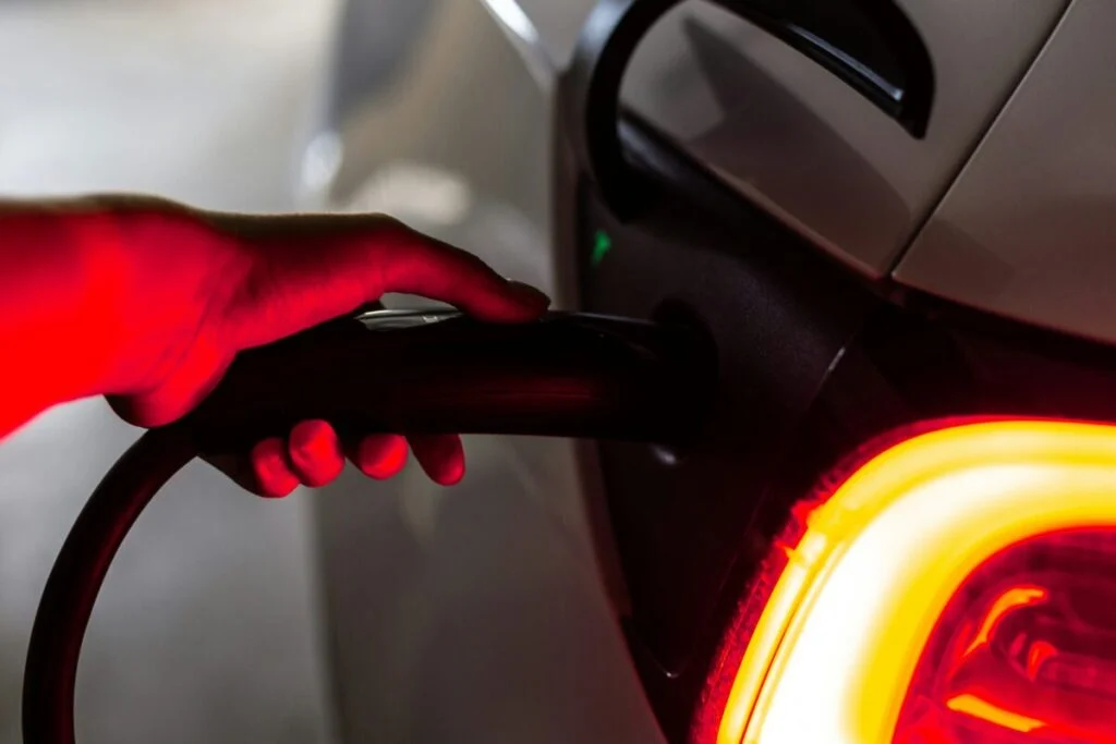 a hand, lit by red light, plugs a car into an EV charger