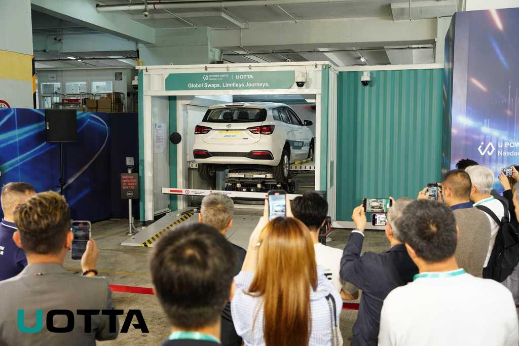 a group of people watch a car lifted into a battery swapping machine
