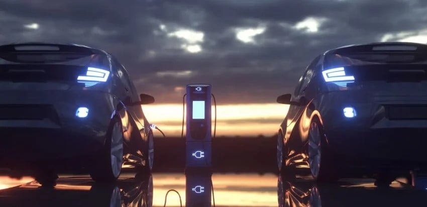 two EVs plugged into a charger at sunset, lit by a neon glow