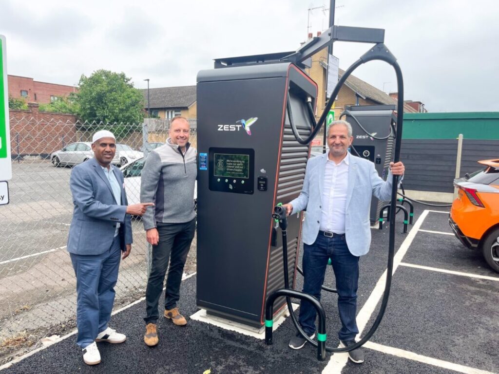 Three men pose next to a large Zest-branded EV charger