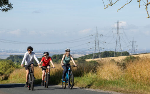 three people ride bikes with pylons behind them