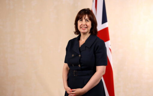 A white woman in a short sleeved black dress stands in front of a Union Flag